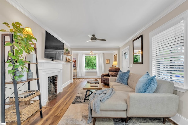 living area with a fireplace with flush hearth, crown molding, a ceiling fan, baseboards, and wood finished floors