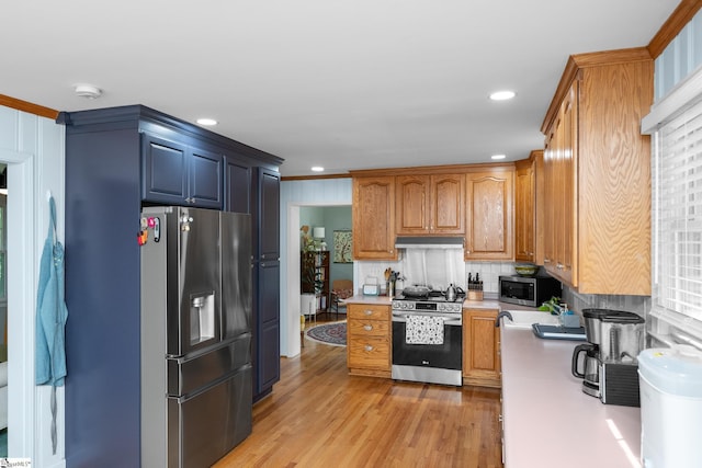 kitchen with tasteful backsplash, under cabinet range hood, appliances with stainless steel finishes, light countertops, and light wood finished floors