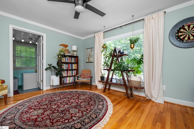 living area with baseboards, ornamental molding, a ceiling fan, and wood finished floors