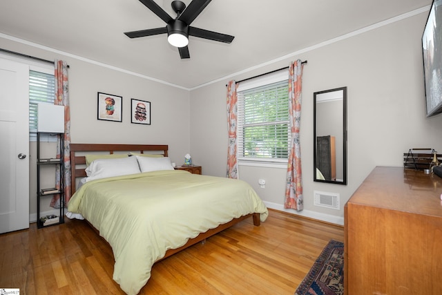 bedroom featuring wood finished floors, visible vents, crown molding, and baseboards