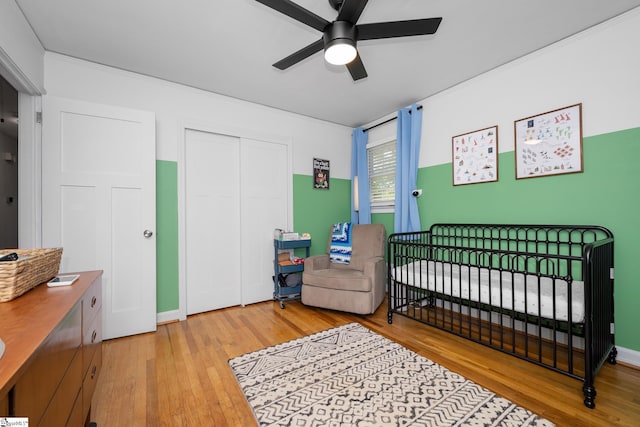 bedroom with a crib, hardwood / wood-style flooring, ceiling fan, and a closet