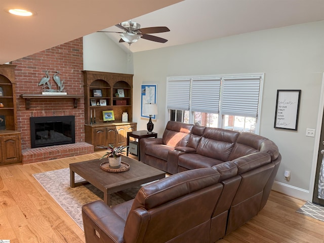 living room with light wood finished floors, ceiling fan, vaulted ceiling, and a fireplace