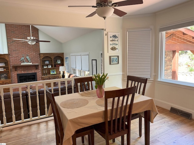 dining area with a fireplace, lofted ceiling, a ceiling fan, visible vents, and wood finished floors