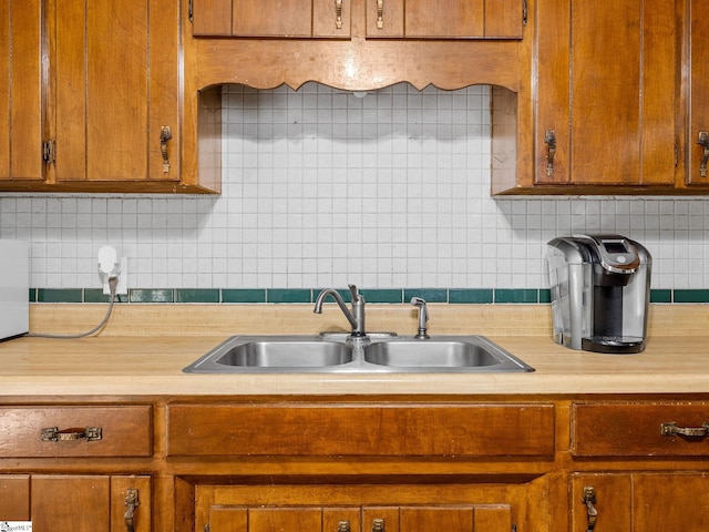 kitchen with backsplash, brown cabinets, light countertops, and a sink