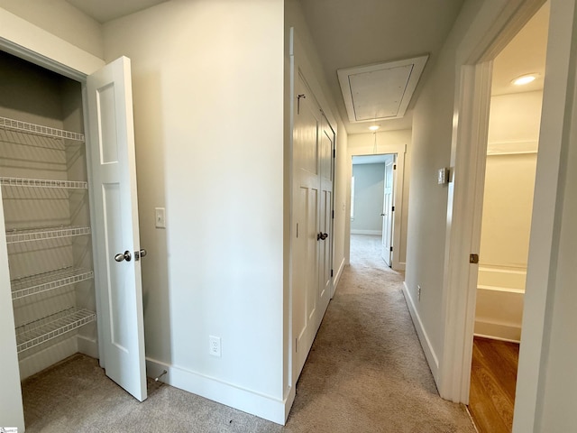 hallway with baseboards, attic access, and light carpet