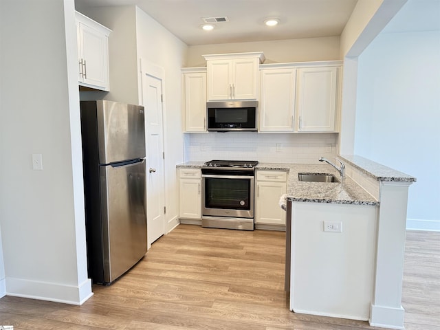 kitchen with a sink, visible vents, stainless steel appliances, light stone countertops, and a peninsula