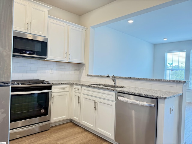 kitchen featuring a sink, light wood-style floors, white cabinetry, a peninsula, and appliances with stainless steel finishes