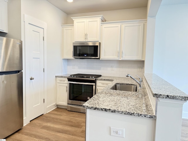 kitchen featuring light wood-style flooring, appliances with stainless steel finishes, white cabinets, a sink, and a peninsula