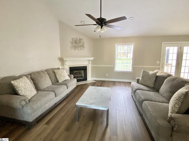 living area featuring vaulted ceiling, ceiling fan, baseboards, a fireplace with flush hearth, and dark wood-type flooring