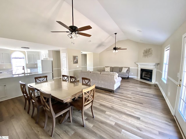 dining space featuring ceiling fan, a fireplace with flush hearth, wood finished floors, and lofted ceiling