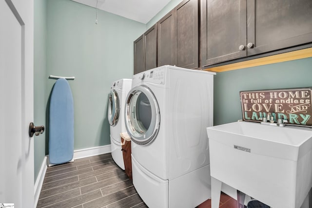 clothes washing area featuring a sink, cabinet space, baseboards, washer and dryer, and dark wood finished floors