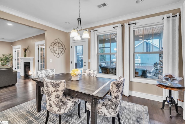 dining area featuring a glass covered fireplace, crown molding, dark wood-type flooring, visible vents, and baseboards