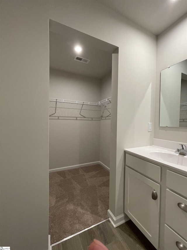 bathroom featuring visible vents, baseboards, wood finished floors, vanity, and a walk in closet