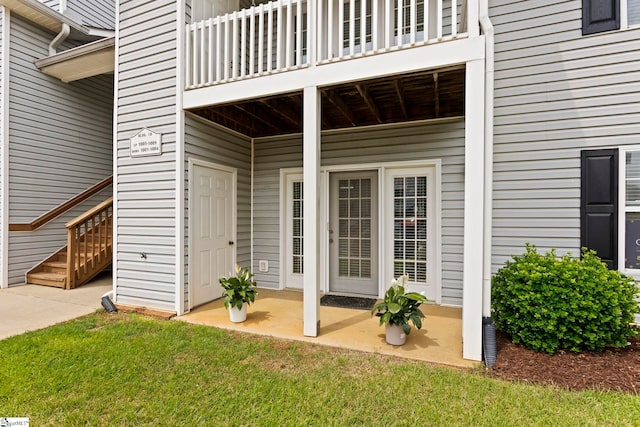 view of exterior entry with a balcony, a yard, and a patio area
