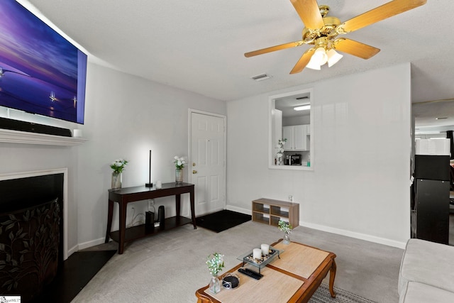 carpeted living area featuring baseboards, visible vents, ceiling fan, and a fireplace