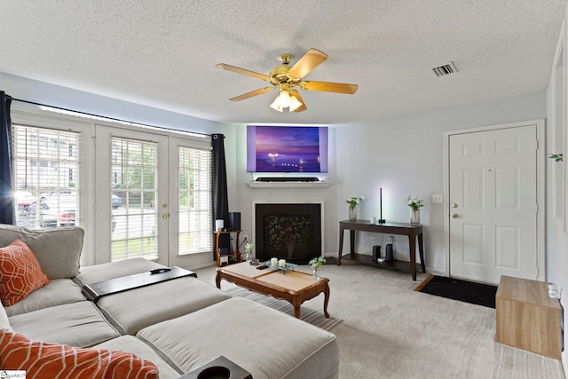 carpeted living room with a fireplace, visible vents, a ceiling fan, a textured ceiling, and french doors