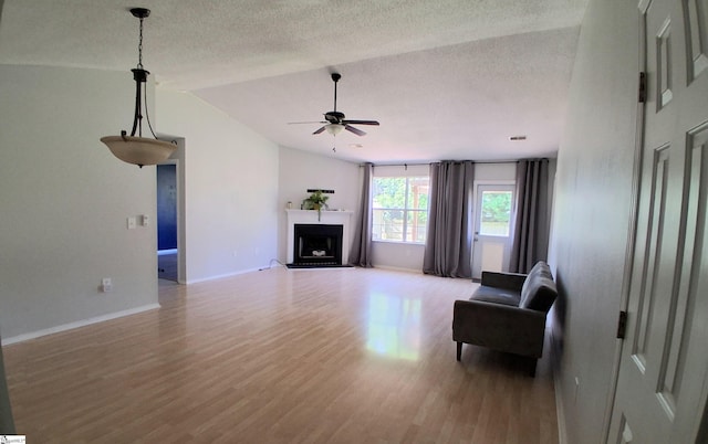 living area with lofted ceiling, a textured ceiling, a fireplace with raised hearth, light wood-type flooring, and a ceiling fan
