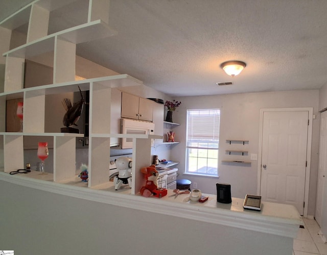 kitchen with light tile patterned floors, open shelves, white microwave, visible vents, and a textured ceiling