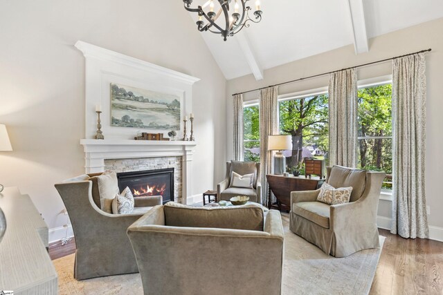 sitting room featuring beam ceiling, a chandelier, light wood-type flooring, and a stone fireplace