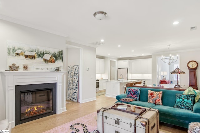 living room featuring light wood-style flooring, visible vents, an inviting chandelier, a glass covered fireplace, and recessed lighting