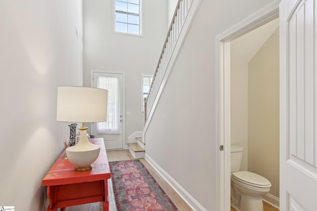 foyer with a towering ceiling, stairs, and light wood-type flooring
