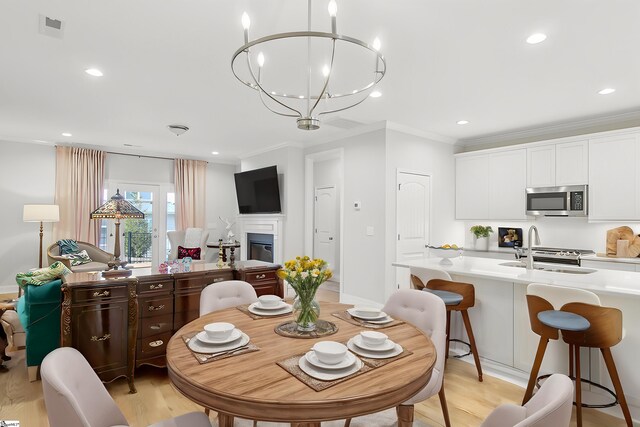 dining space featuring an inviting chandelier, a glass covered fireplace, light wood-type flooring, recessed lighting, and ornamental molding