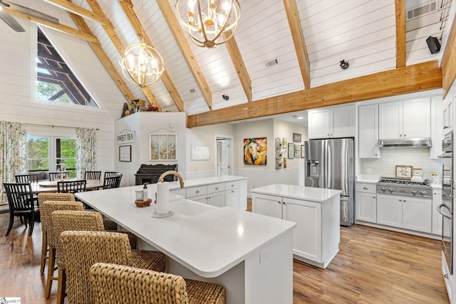 kitchen with a sink, stainless steel appliances, a chandelier, a large island, and high vaulted ceiling