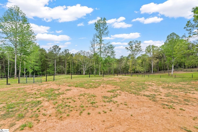 view of yard featuring fence, a wooded view, and a rural view