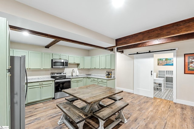 kitchen with beamed ceiling, a sink, a barn door, stainless steel appliances, and green cabinets