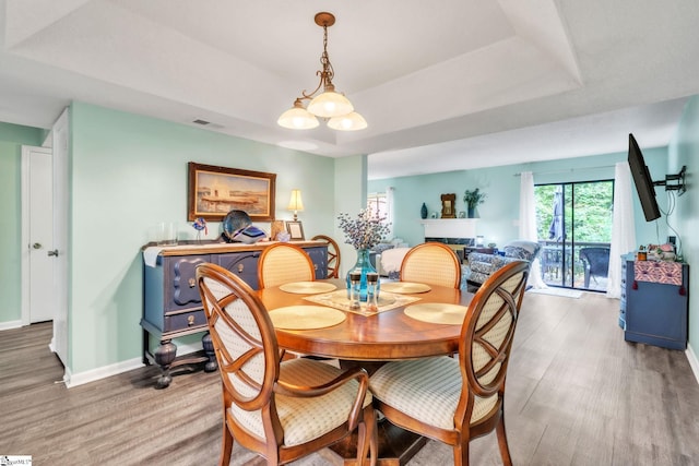 dining area featuring light wood-style floors, a tray ceiling, visible vents, and baseboards