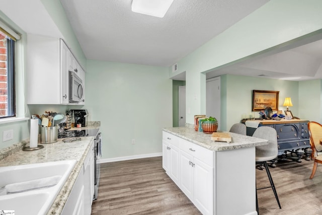 kitchen with a breakfast bar, light wood-style floors, appliances with stainless steel finishes, and white cabinetry