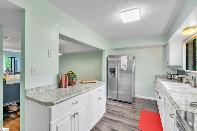 kitchen featuring wood finished floors, light countertops, a sink, white cabinetry, and stainless steel refrigerator with ice dispenser