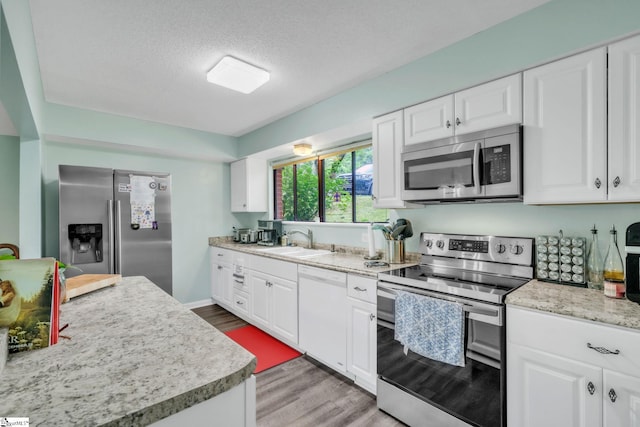 kitchen featuring light wood-style flooring, stainless steel appliances, light countertops, a sink, and white cabinetry