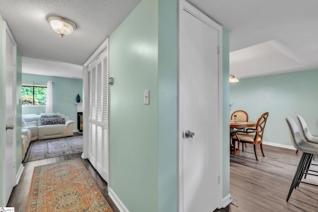 corridor featuring a textured ceiling, wood finished floors, and baseboards