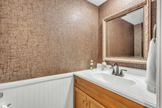 bathroom featuring a wainscoted wall, wallpapered walls, and vanity