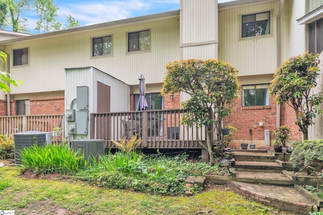 rear view of property featuring cooling unit, a wooden deck, and brick siding