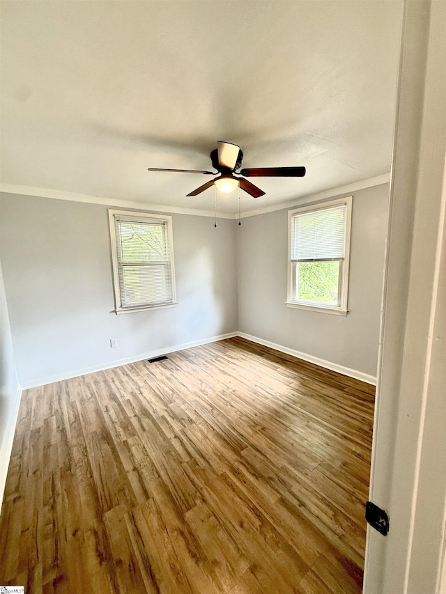 empty room featuring wood finished floors, a ceiling fan, crown molding, and plenty of natural light