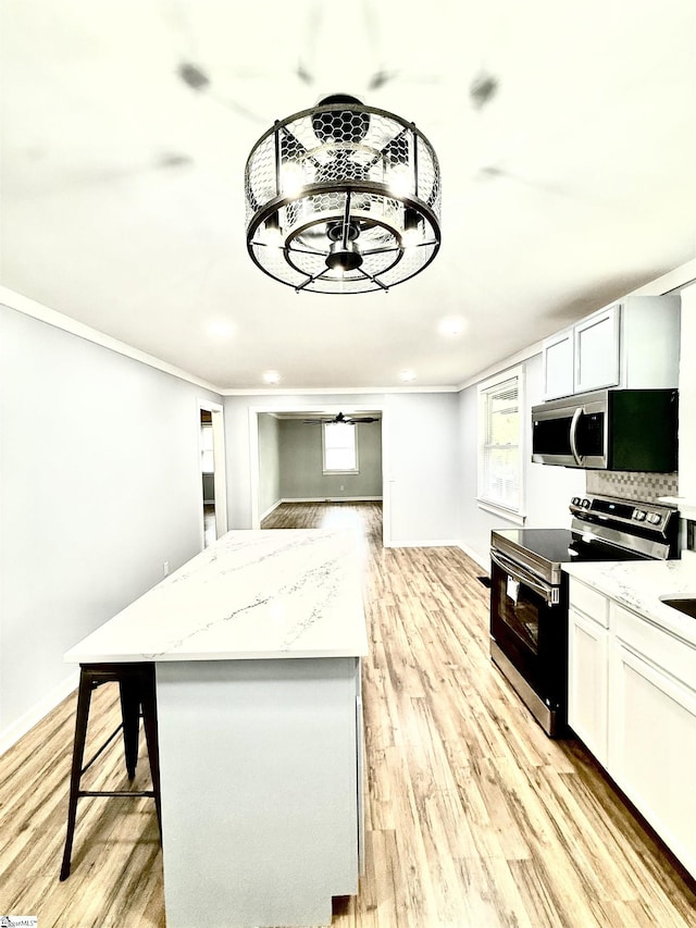 kitchen featuring light stone countertops, a center island, light wood-style flooring, ornamental molding, and appliances with stainless steel finishes