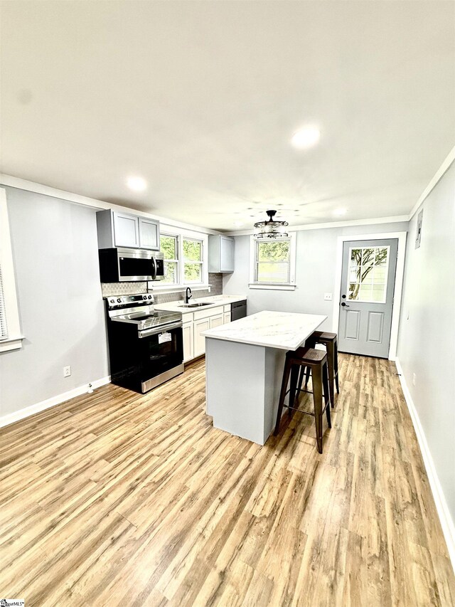 kitchen with light wood finished floors, a sink, a center island, a breakfast bar, and appliances with stainless steel finishes