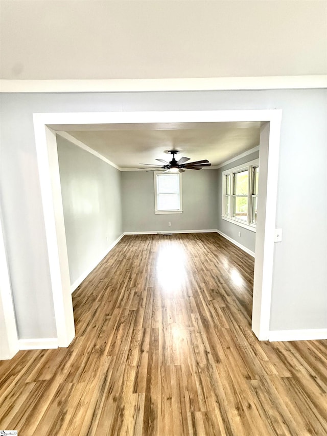 unfurnished room with wood finished floors, a ceiling fan, ornamental molding, and baseboards