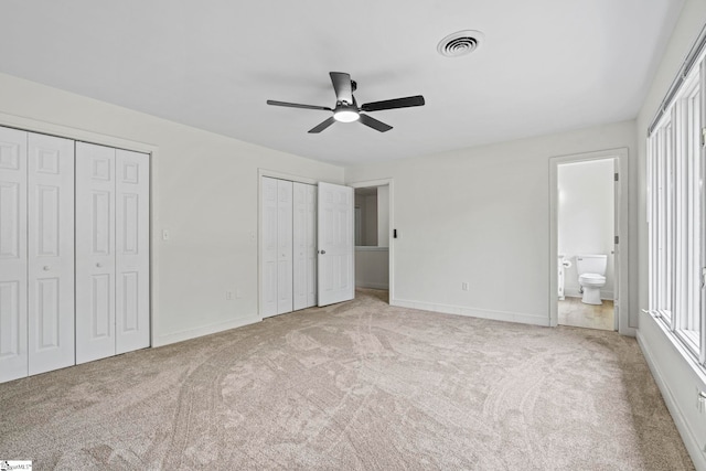 unfurnished bedroom with visible vents, two closets, carpet flooring, and baseboards