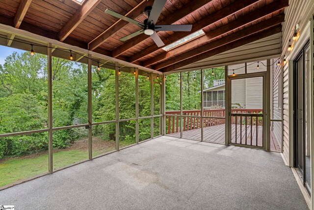 unfurnished sunroom with beam ceiling, a ceiling fan, and a skylight