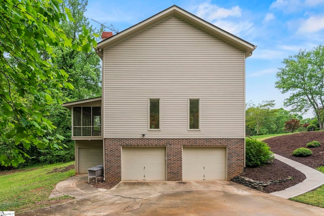 view of property exterior featuring driveway, a sunroom, brick siding, and a garage