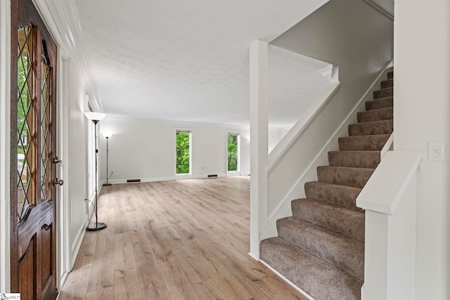entryway featuring a textured ceiling, stairway, baseboards, light wood-type flooring, and ornamental molding