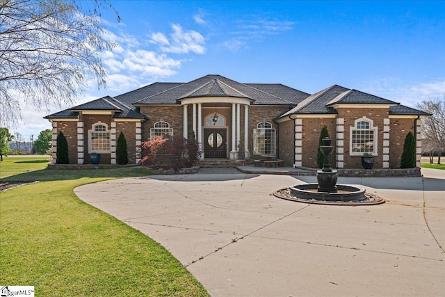 neoclassical home featuring a shingled roof, brick siding, curved driveway, and a front yard