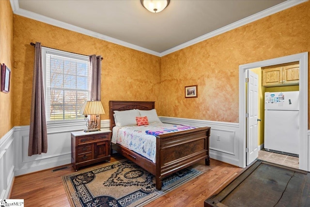 bedroom with wood finished floors, ornamental molding, and freestanding refrigerator