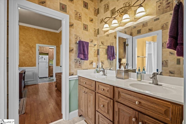 full bath with wallpapered walls, double vanity, ornamental molding, a wainscoted wall, and a sink