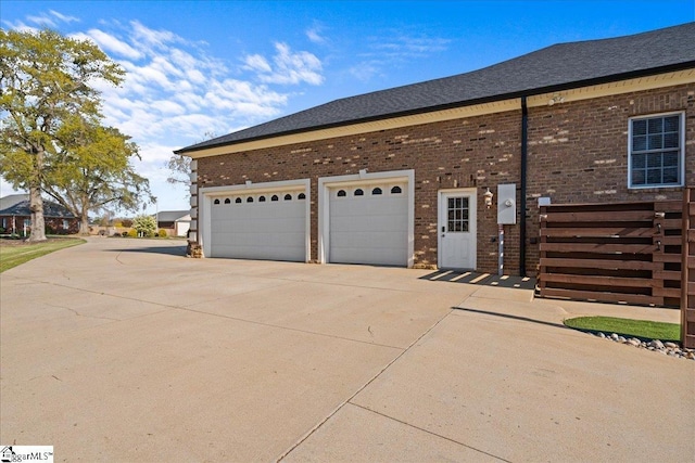 view of side of home featuring concrete driveway, a shingled roof, and brick siding