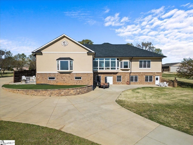 view of front of home featuring a front yard, stucco siding, brick siding, and a patio area
