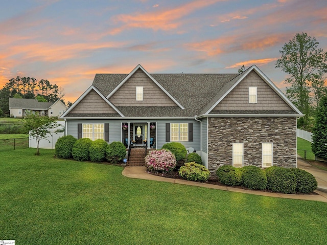 craftsman-style house with fence, roof with shingles, a front lawn, and stone siding
